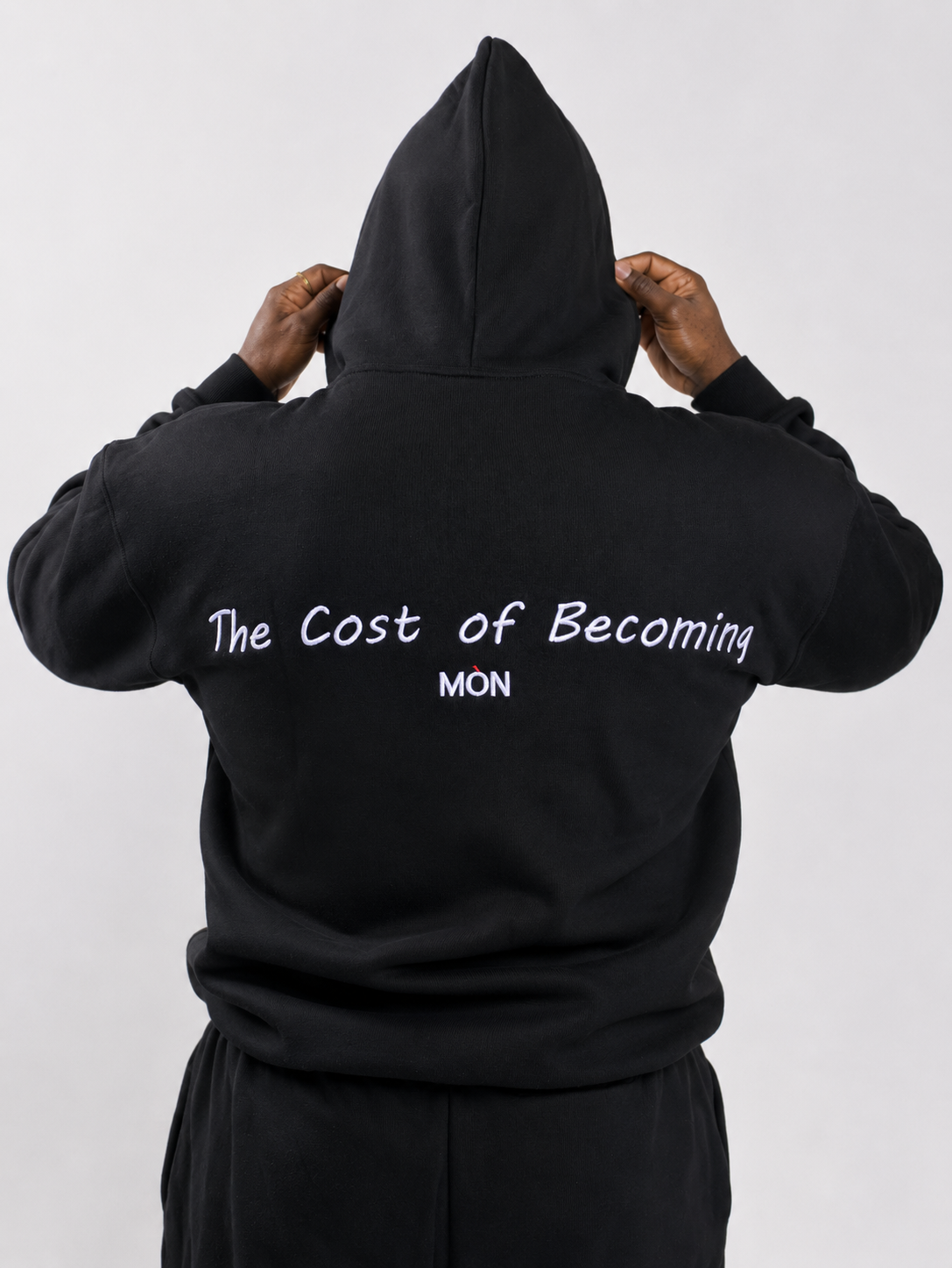 MÒN The Summit Hoodie in black, hood up back view with "The Cost of Becoming" embroidery
